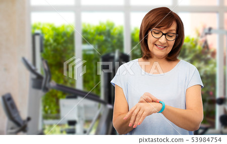 smiling senior woman with fitness tracker in gym smiling senior woman with fitness tracker in gym 53984754