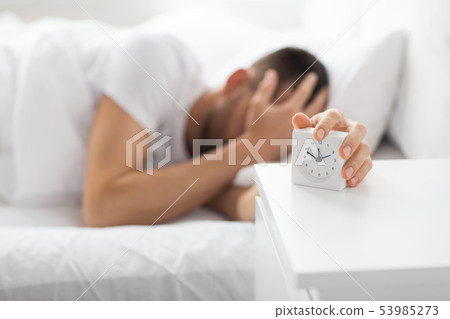 close up of man in bed reaching for alarm clock close up of man in bed reaching for alarm clock 53985273