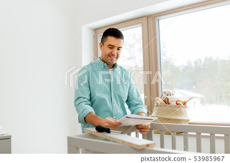 father with manual assembling baby bed at home 53985967