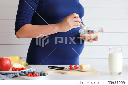 pregnant woman eat a bowl of yogurt and fruits  53985969