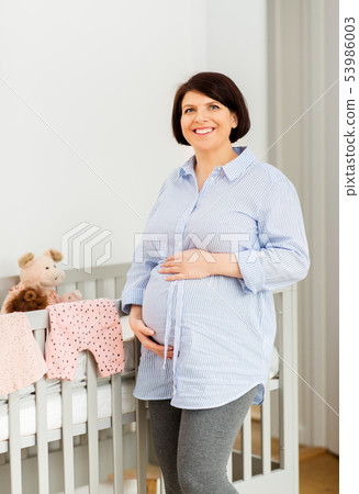 happy pregnant woman next to baby bed at home 53986003