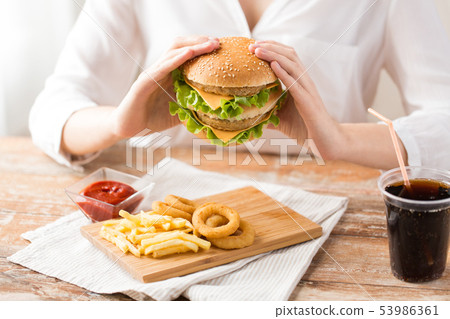 close up of woman eating hamburger at restaurant 53986361