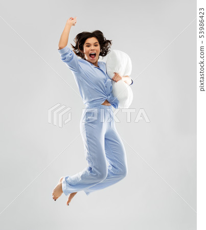 happy woman in blue pajama jumping with pillow happy woman in blue pajama jumping with pillow 53986423