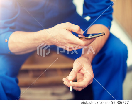 auto mechanic smoking cigarette at car workshop auto mechanic smoking cigarette at car workshop 53986777