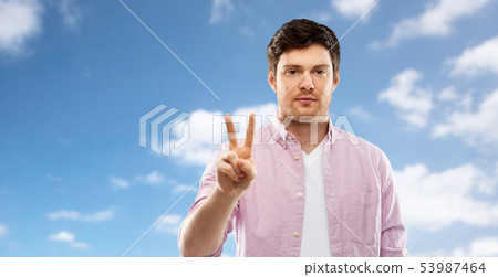 young man showing two fingers over sky young man showing two fingers over sky 53987464