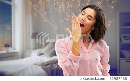 happy young sleepy woman in pajama yawning 53987486