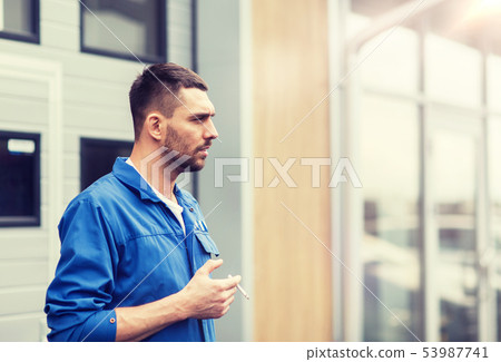 auto mechanic smoking cigarette at car workshop auto mechanic smoking cigarette at car workshop 53987741