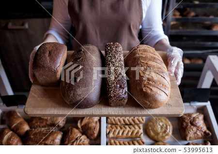 Seller holding a tray with fresh loaf of different bread 53995613