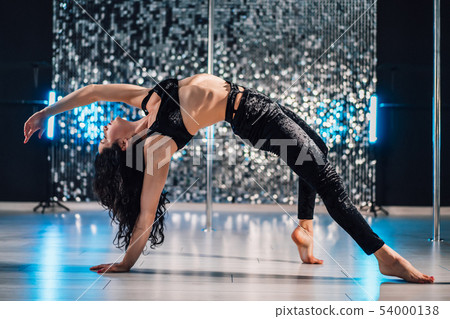Woman doing tricks, practicing in studio with pylon.Young stripper in black Woman doing tricks, practicing in studio with pylon.Young stripper in black 54000138