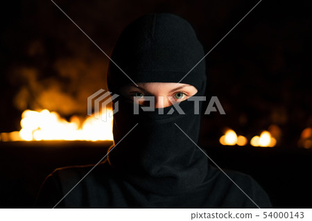 Portrait of female protesting activist in balaclava near barricades at night Portrait of female protesting activist in balaclava near barricades at night 54000143