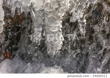 Icicles forming in flowing river small waterfall 54000311