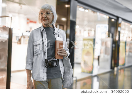 Smiling senior lady staying at hall with camera Smiling senior lady staying at hall with camera 54002000