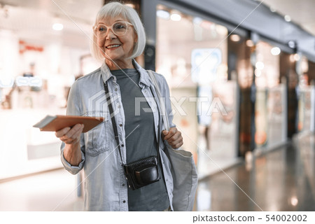 Smiling senior lady with bag staying at hall near shop Smiling senior lady with bag staying at hall near shop 54002002