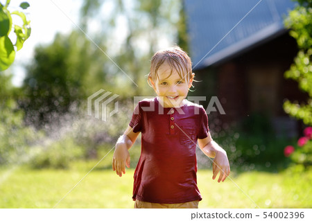 Funny little boy playing with garden sprinkler in 54002396