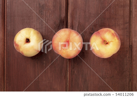 An overhead photo of vibrant organic flat saturn peaches on a dark rustic wooden background with An overhead photo of vibrant organic flat saturn peaches on a dark rustic wooden background with 54011206