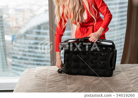 Close-up unpacks suitcase Young blond businesswoman arrives in a hotel room with black suitcase Close-up unpacks suitcase Young blond businesswoman arrives in a hotel room with black suitcase 54019260