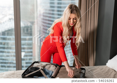 Young girl packs suitcase. Fashionable blond businesswoman arrives in a hotel room with black Young girl packs suitcase. Fashionable blond businesswoman arrives in a hotel room with black 54019261