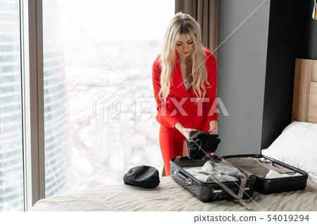 Stewardess in red uniform arrives in a hotel room with black suitcase. Rest in the transit city 54019294