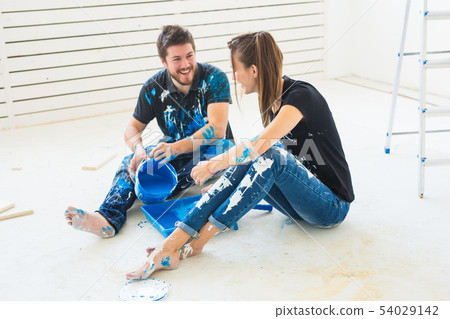 Renovation, redecoration and interiors concept - Young couple sitting on the white floor and pour Renovation, redecoration and interiors concept - Young couple sitting on the white floor and pour 54029142