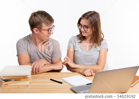 People and education concept - Two happy funny students sitting at the wooden table with laptop and 54029192