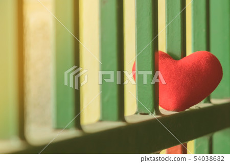 A little red heart pillow on a green steel fence. 54038682