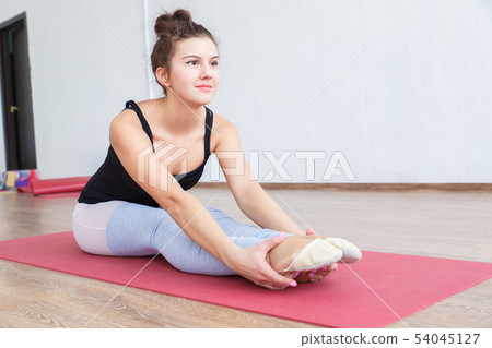 Young and slender girl doing stretching muscles and ligaments on the Mat in the gym. 54045127