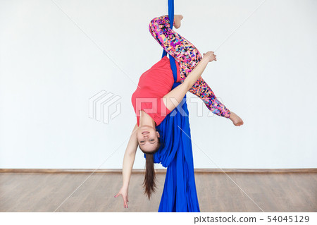Young girl gymnast hanging on the canvases of cloth in the dance Studio in front of a white wall. Young girl gymnast hanging on the canvases of cloth in the dance Studio in front of a white wall. 54045129