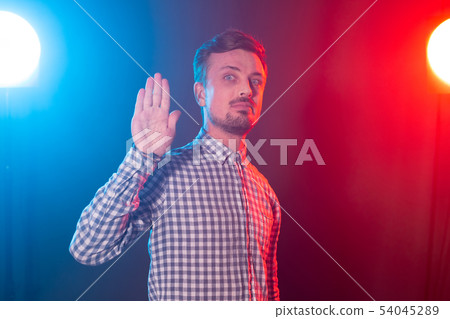 Serious young bearded handsome hipster man shows palm up portraying stop on blue-red background 54045289