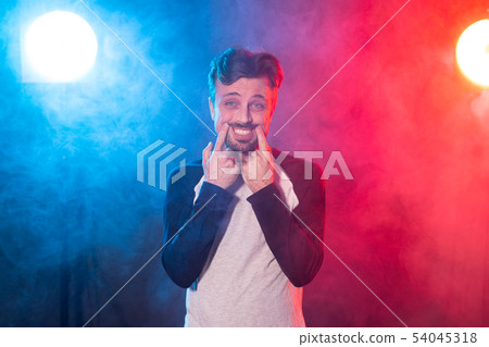 Funny young man with a beard in casual clothes pulls a smile with his hands posing on a red blue 54045318