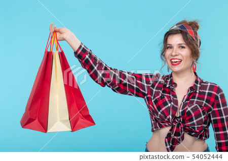 Positive young beautiful woman in a plaid shirt and holding shopping bags. Concept of new purchases Positive young beautiful woman in a plaid shirt and holding shopping bags. Concept of new purchases 54052444