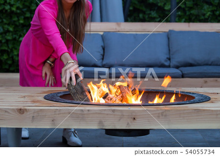 woman throws logs on fire pit in the garden on a summer day woman throws logs on fire pit in the garden on a summer day 54055734