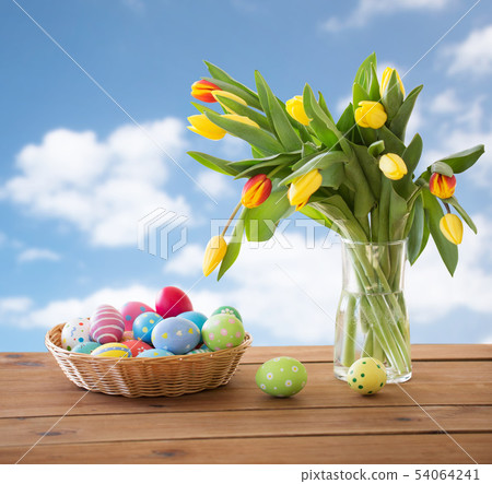 colored easter eggs in basket and flowers over sky colored easter eggs in basket and flowers over sky 54064241