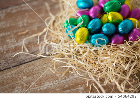 chocolate eggs in foil wrappers in straw nest 54064292