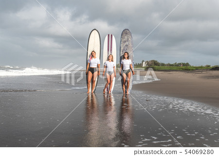 Girls surfers stand with boards on the beach. Girls surfers stand with boards on the beach. 54069280