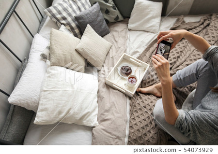 Woman taking shot of tray with food on bed 54073929