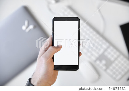 Left hand holding a mobile phone over the desk Left hand holding a mobile phone over the desk 54075281