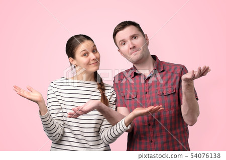Uncertain couple shrugging shoulders isolated over pink background 54076138