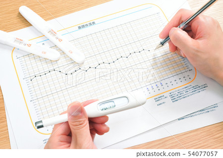 Hand of woman to fill in basal body temperature table 54077057