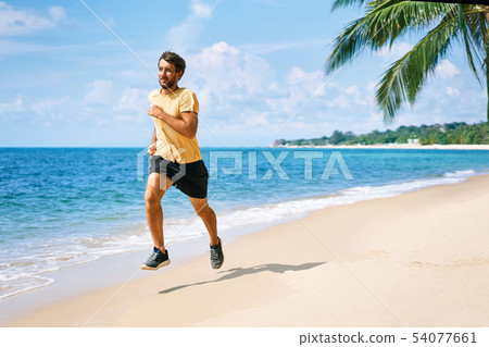 Young man running on the sea shore of tropical beach Young man running on the sea shore of tropical beach 54077661