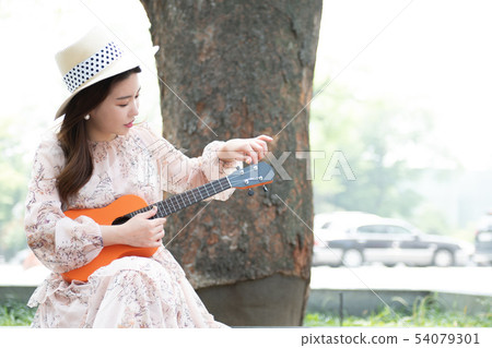 Woman tuning ukulele under a tree Woman tuning ukulele under a tree 54079301