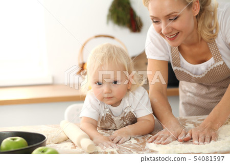 Little girl and her blonde mom in beige aprons playing and laughing while kneading the dough in Little girl and her blonde mom in beige aprons playing and laughing while kneading the dough in 54081597
