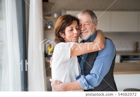 Affectionate senior couple in love standing indoors at home, hugging. Affectionate senior couple in love standing indoors at home, hugging. 54082072