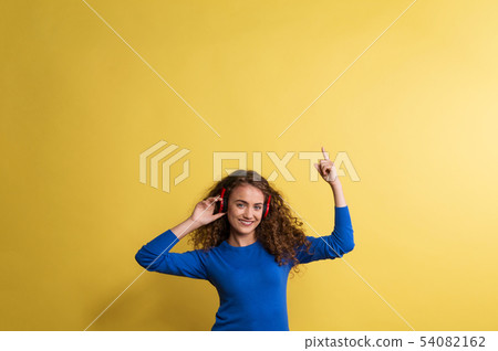 Portrait of a young woman with headphones in a studio on a yellow background. 54082162