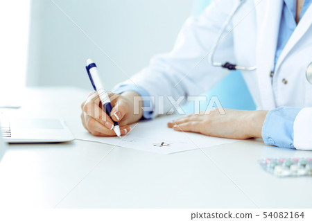 Female doctor filling up prescription form while sitting at the desk in hospital closeup. Healthcare Female doctor filling up prescription form while sitting at the desk in hospital closeup. Healthcare 54082164