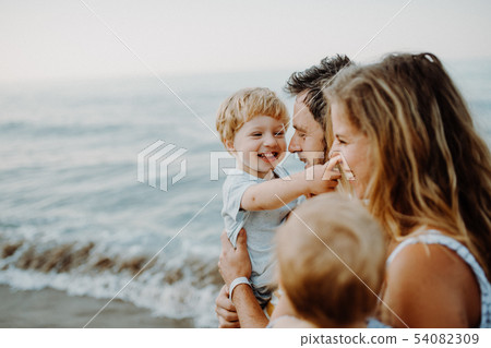 A young family with two toddler children standing on beach on summer holiday. A young family with two toddler children standing on beach on summer holiday. 54082309