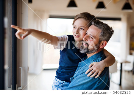 Mature father holding small son indoors, looking out of window. Mature father holding small son indoors, looking out of window. 54082535
