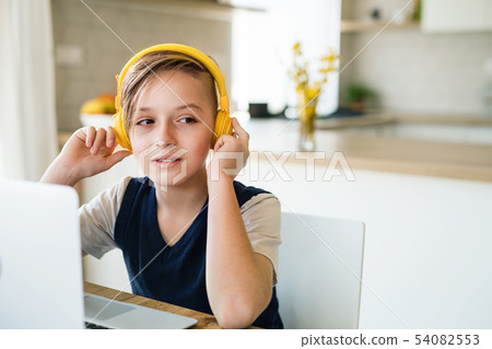 Small boy with headphones and laptop sitting at the table indoors at home. Small boy with headphones and laptop sitting at the table indoors at home. 54082553