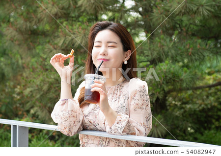 A woman who drinks coffee with sweets in the forest and closes her eyes and smiles 54082947