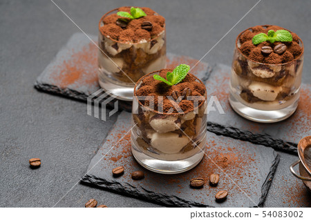 Classic tiramisu dessert in a glass on stone serving board on dark concrete background Classic tiramisu dessert in a glass on stone serving board on dark concrete background 54083002