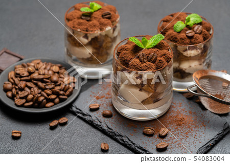 Classic tiramisu dessert in a glass on stone serving board on dark concrete background Classic tiramisu dessert in a glass on stone serving board on dark concrete background 54083004